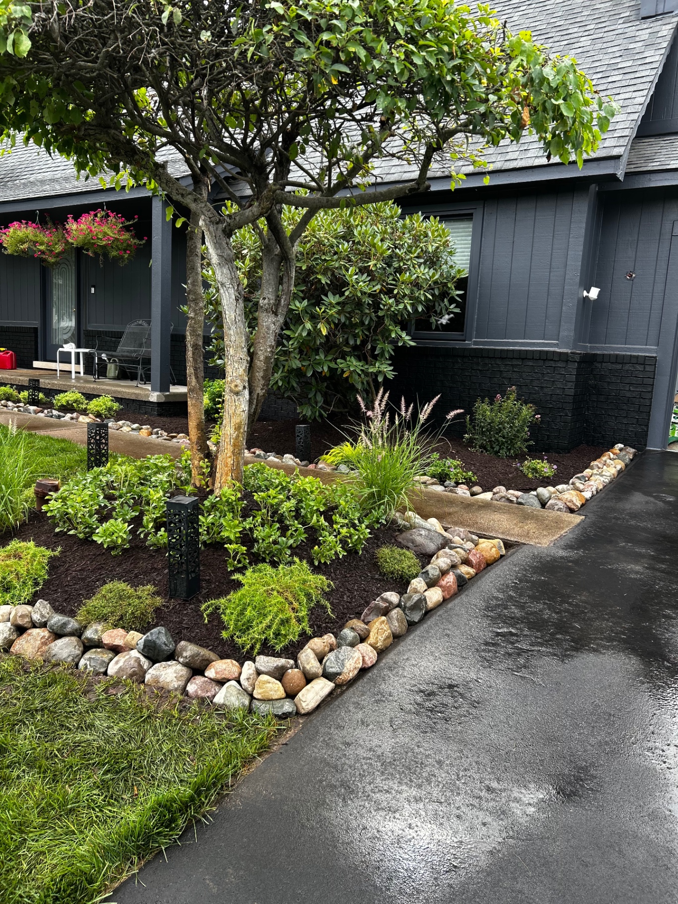 Curved stone border, layered shrubs and path lighting along the walkway.