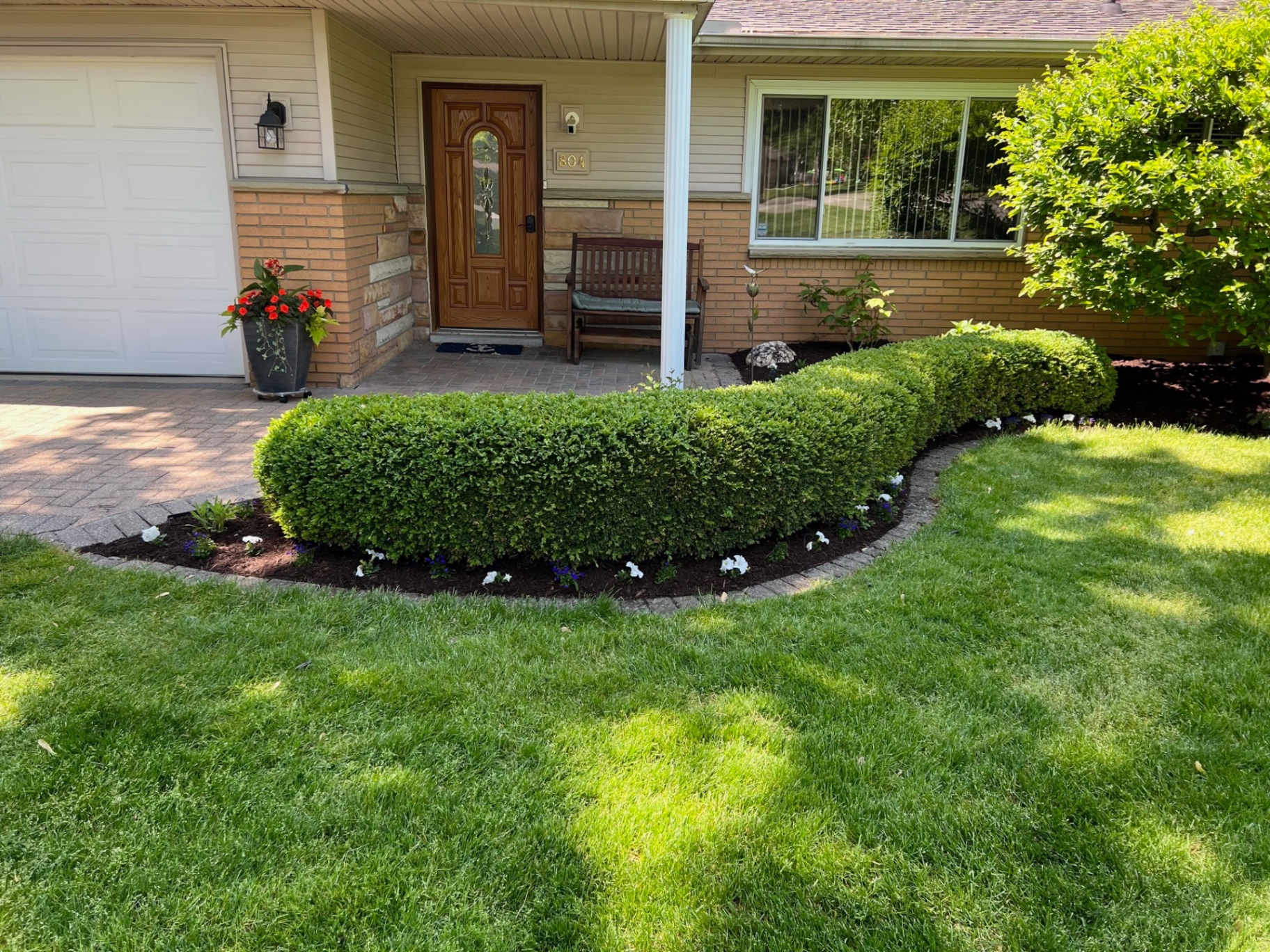 Carefully shaped boxwoods, seasonal flowers, and clean mulch beds around a welcoming front entry.