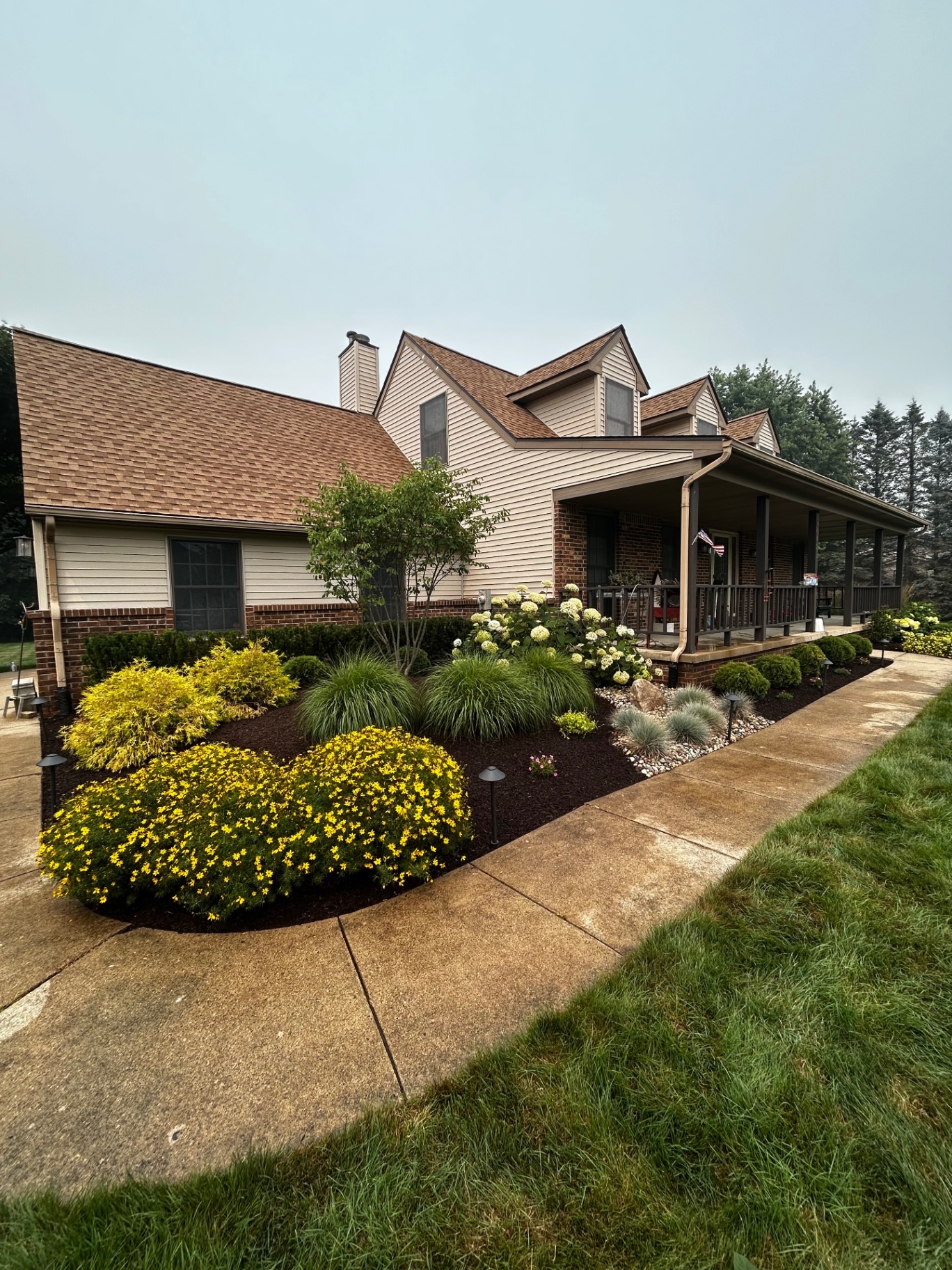 Colorful front-yard planting with dark mulch, stone edging, and a curved walkway in Oakland County, MI.